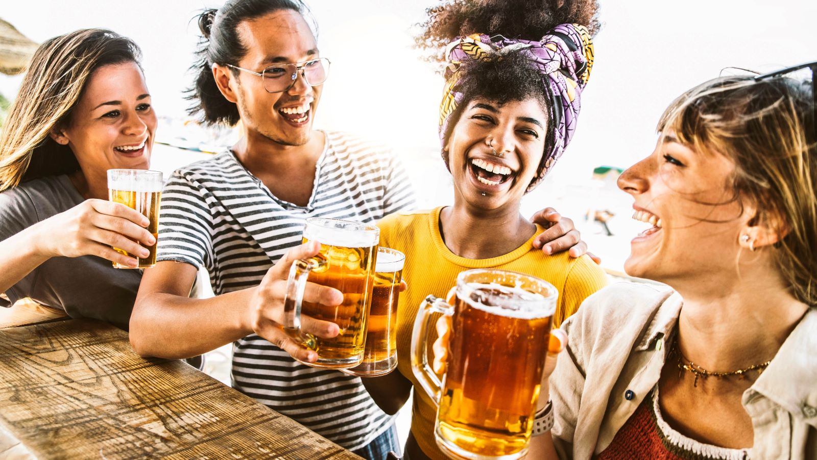A group of four friends laugh and drink beer together.